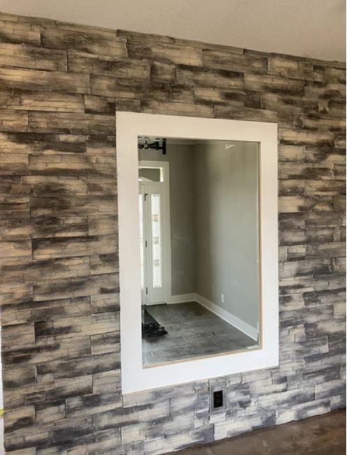Mirror mounted on a gray stone-pattern accent wall in an empty room with white trim.