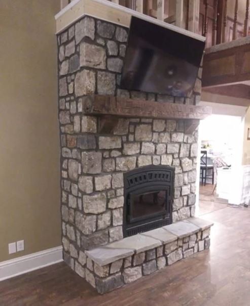 Stone fireplace with a black metal firebox and raised hearth in a home interior.