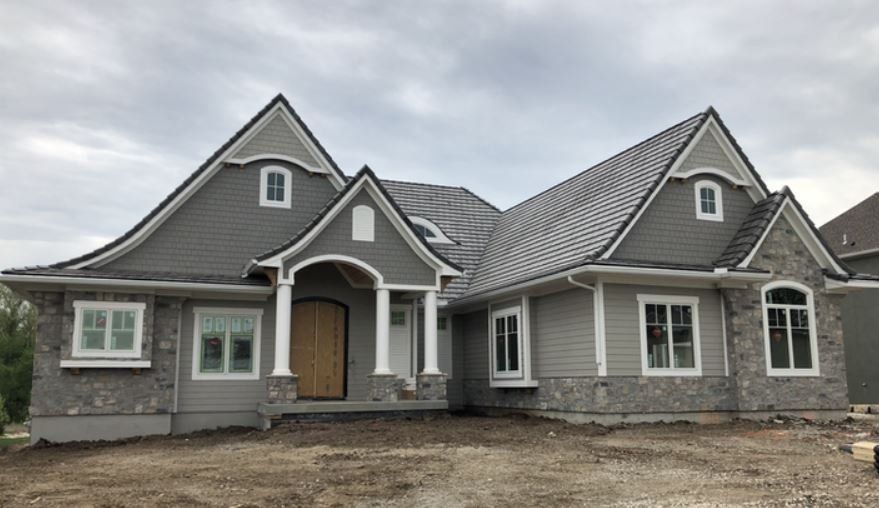 Gray two-story house with gabled roof, stone facade, and arched front entry under cloudy skies
