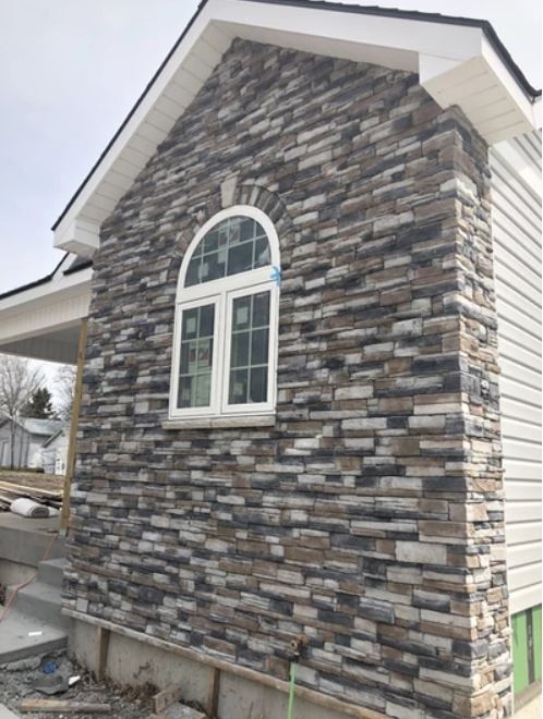 Stone veneer exterior wall with arched window and white siding on a house
