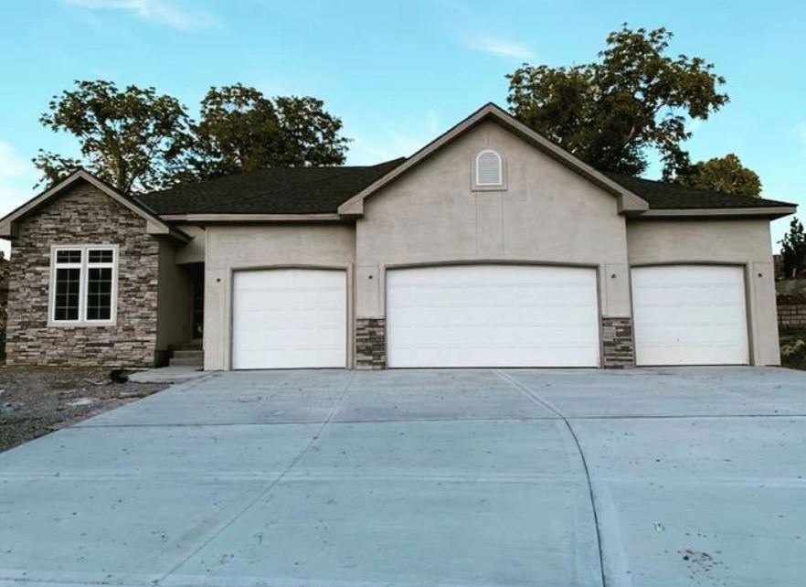 Suburban house with three garage doors and a wide concrete driveway at dusk