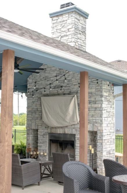 Outdoor stone fireplace on a covered patio with wicker seating and a chimney.