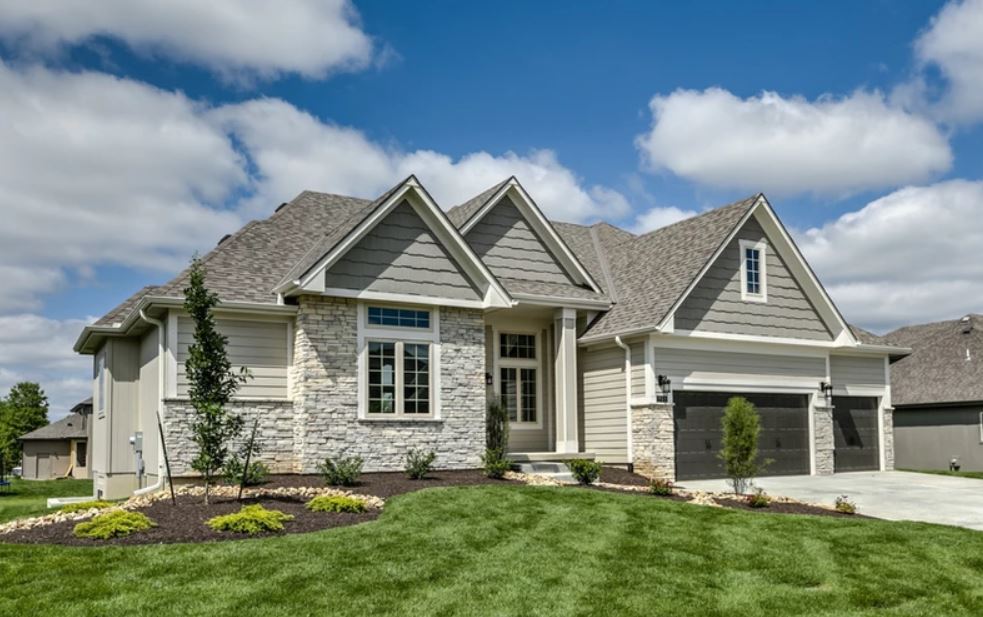Single-story suburban house with stone exterior, gabled roof, and well-kept green lawn under a blue sky