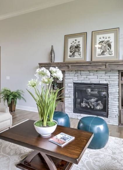 Modern living room with stone fireplace, framed art, and a coffee table with white flowers in the foreground