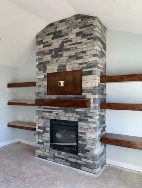 Modern stone fireplace with wooden mantel shelves in a bright, empty room