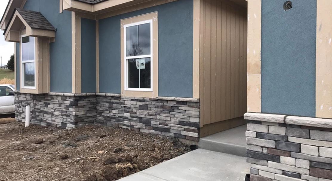 New home's exterior with tan siding, blue panels, and stone veneer along a concrete walkway