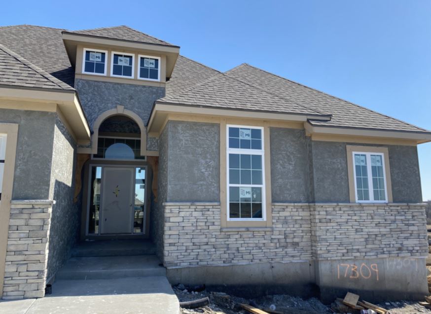 Front view of a gray stone and stucco house with arched entry and blue sky