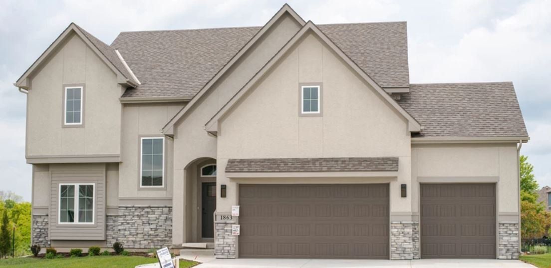 Suburban two-story beige house with stone accents and a large brown garage door.