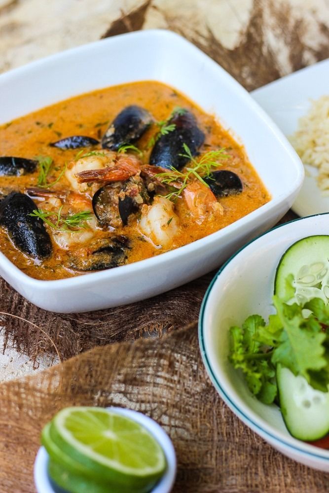 Seafood stew in white bowl, with rice, and salad. Orange-red broth with mussels and shrimp.
