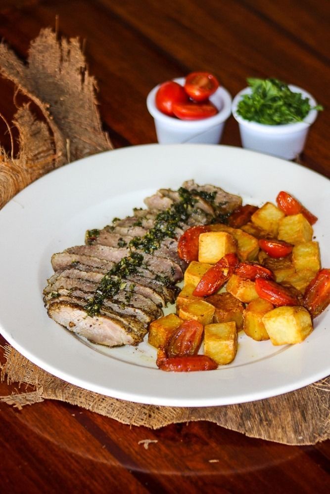 Sliced meat topped with herbs, roasted potatoes, and tomatoes on a white plate.