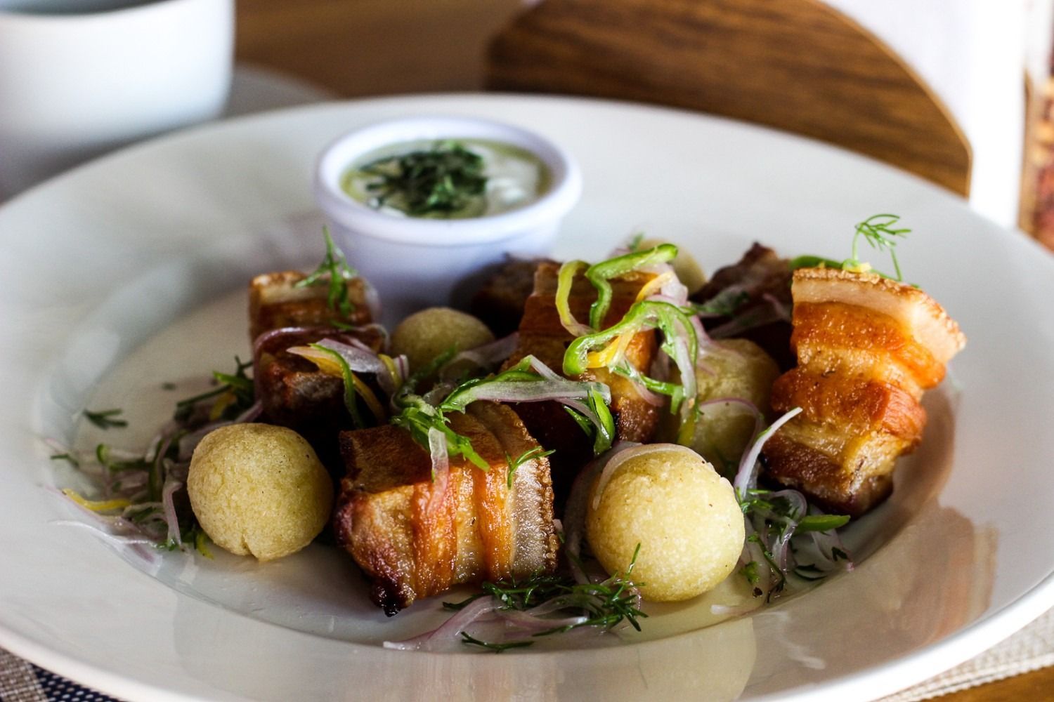 Plate of pork belly cubes, potato balls, onions, and sauce.