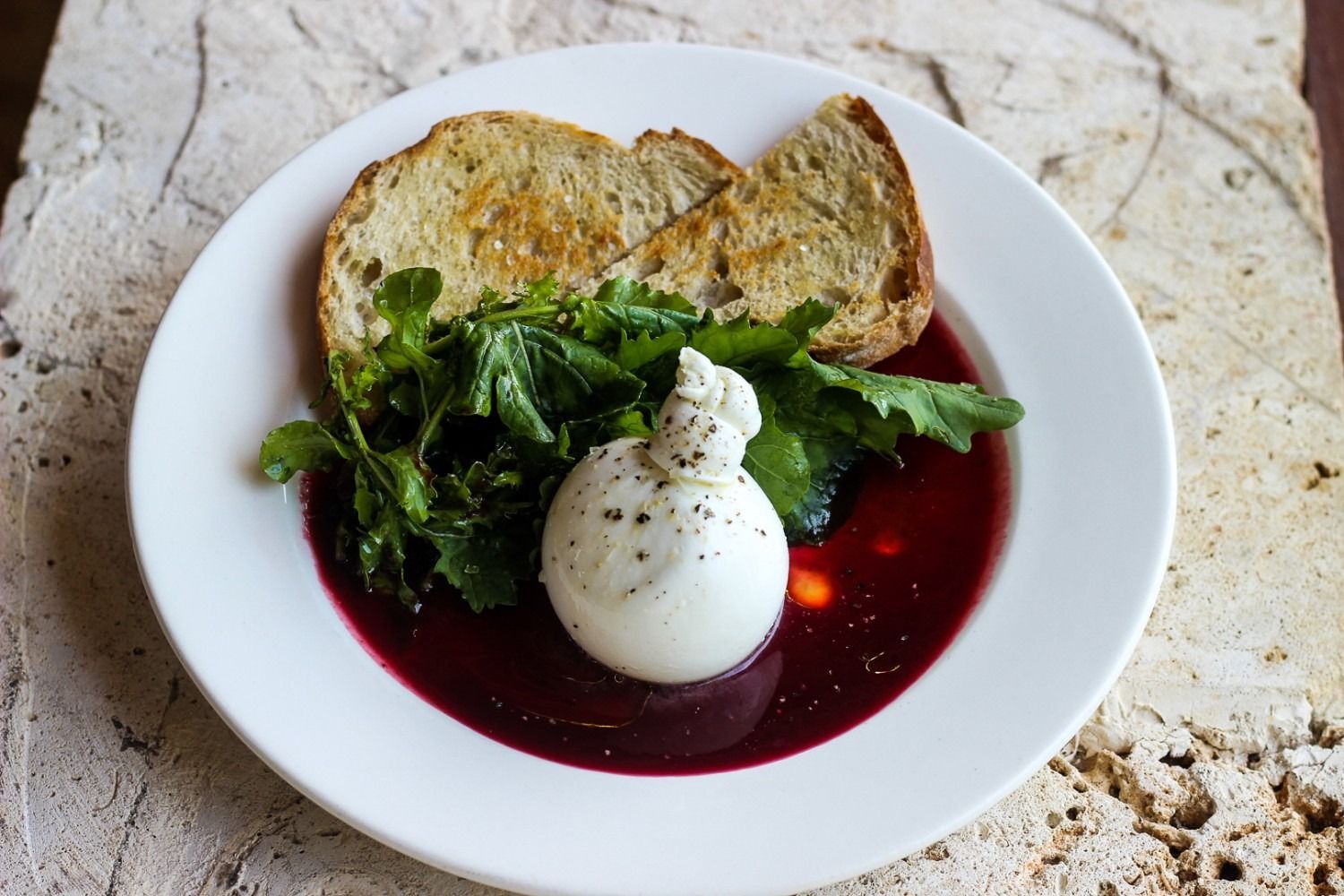 Burrata cheese on a plate with red sauce, greens, and toasted bread.