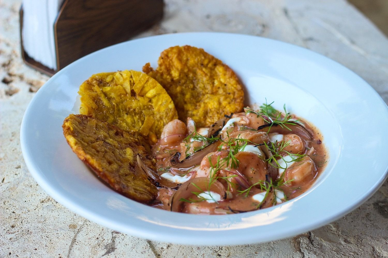 Plate of shrimp dish with fried plantains, on a beige surface.