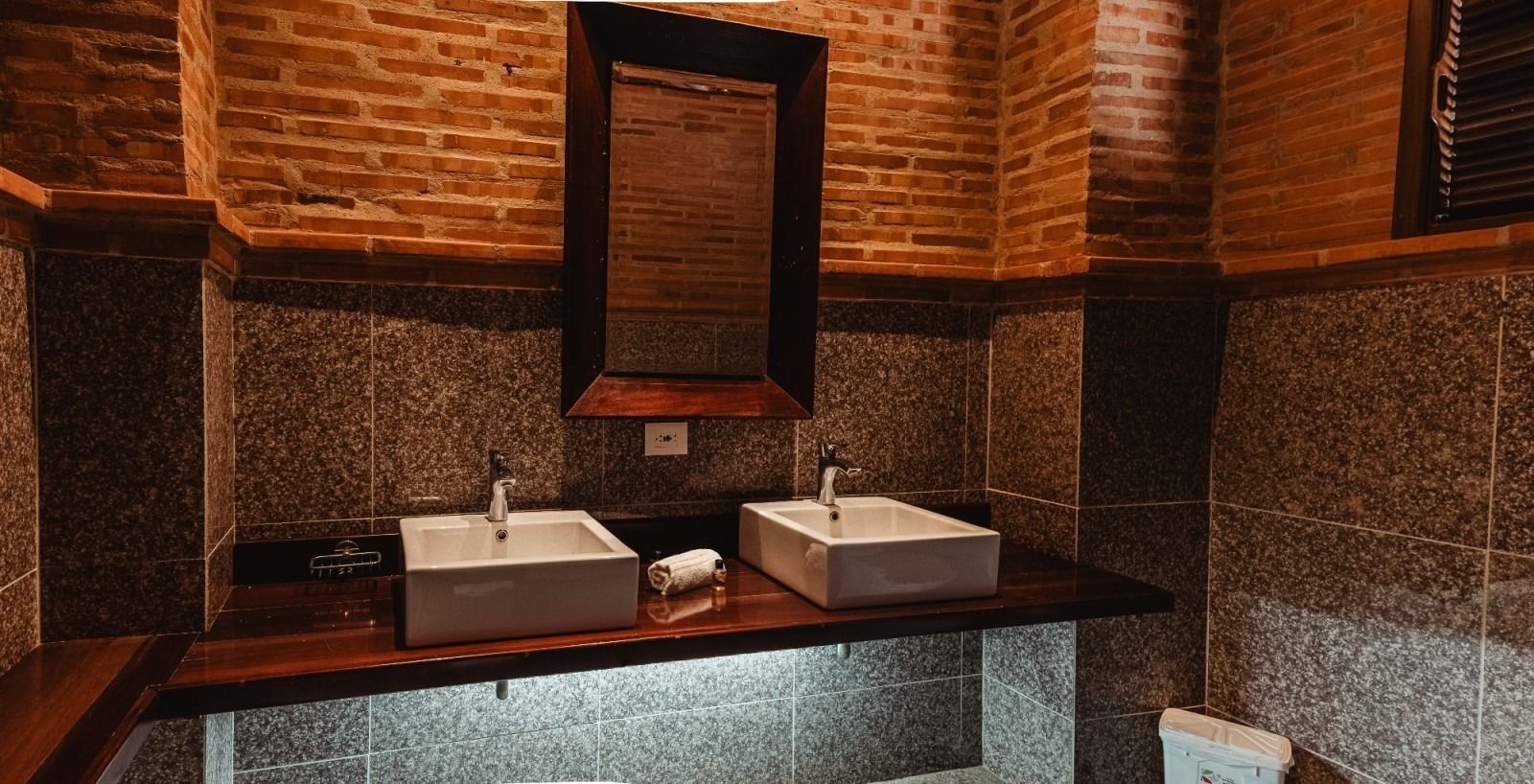 Bathroom with brick walls, two white sinks on a wooden counter, and a large mirror.