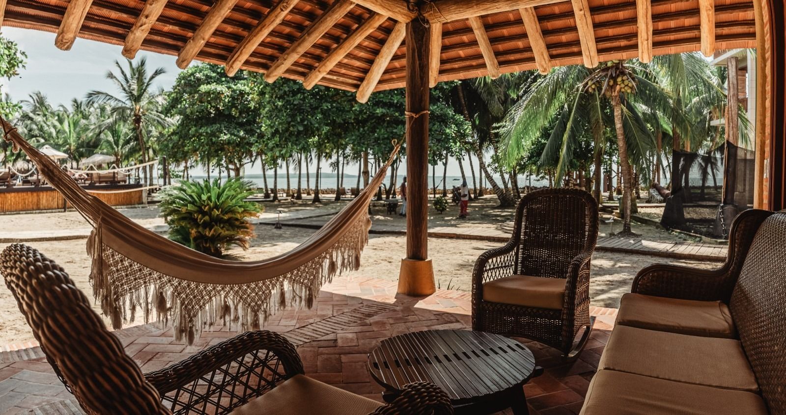 Patio with hammock and wicker furniture, overlooking beach with palm trees.