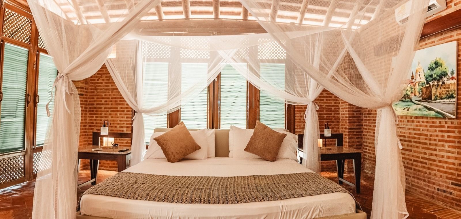 Bedroom with canopy bed, brick walls, and artwork; window view in the background.