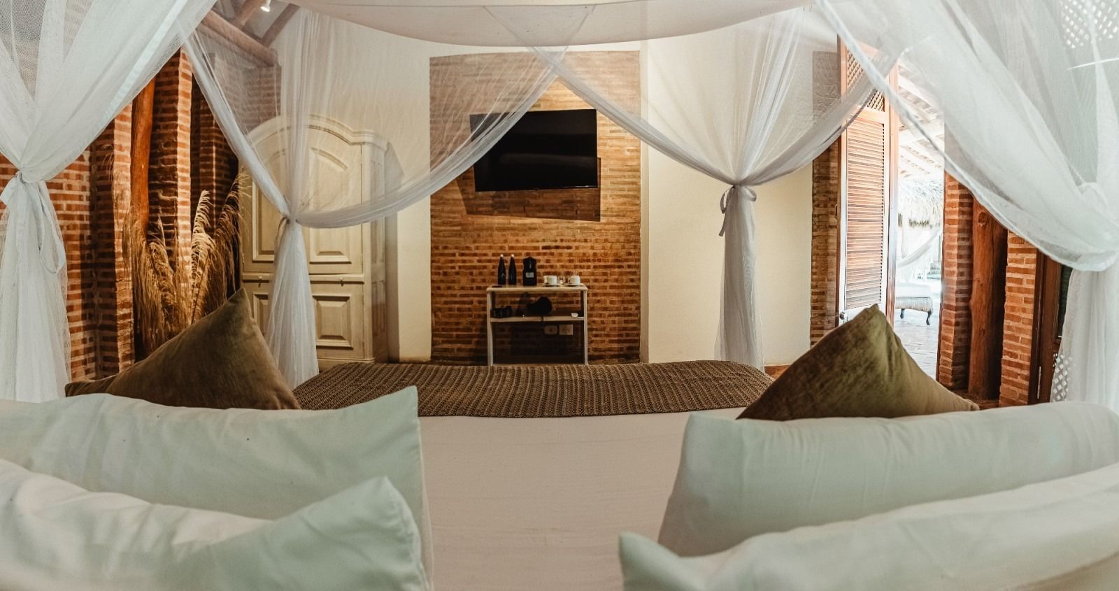 Bedroom with bed, mosquito net, brick wall, TV, open doors.
