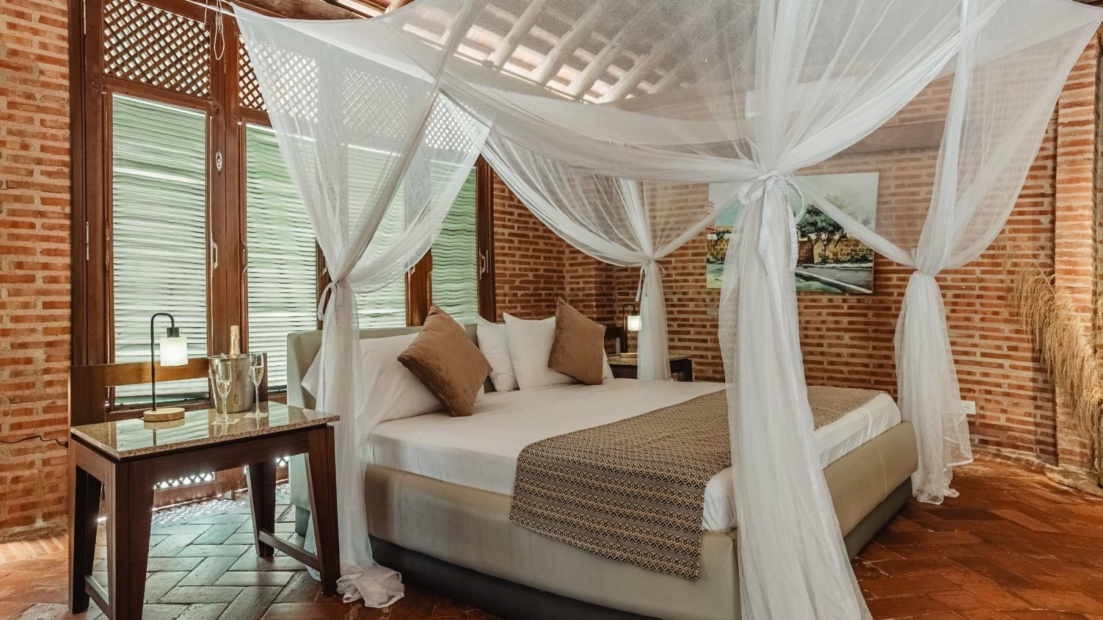 Bedroom with canopy bed, brick walls, and small side table.