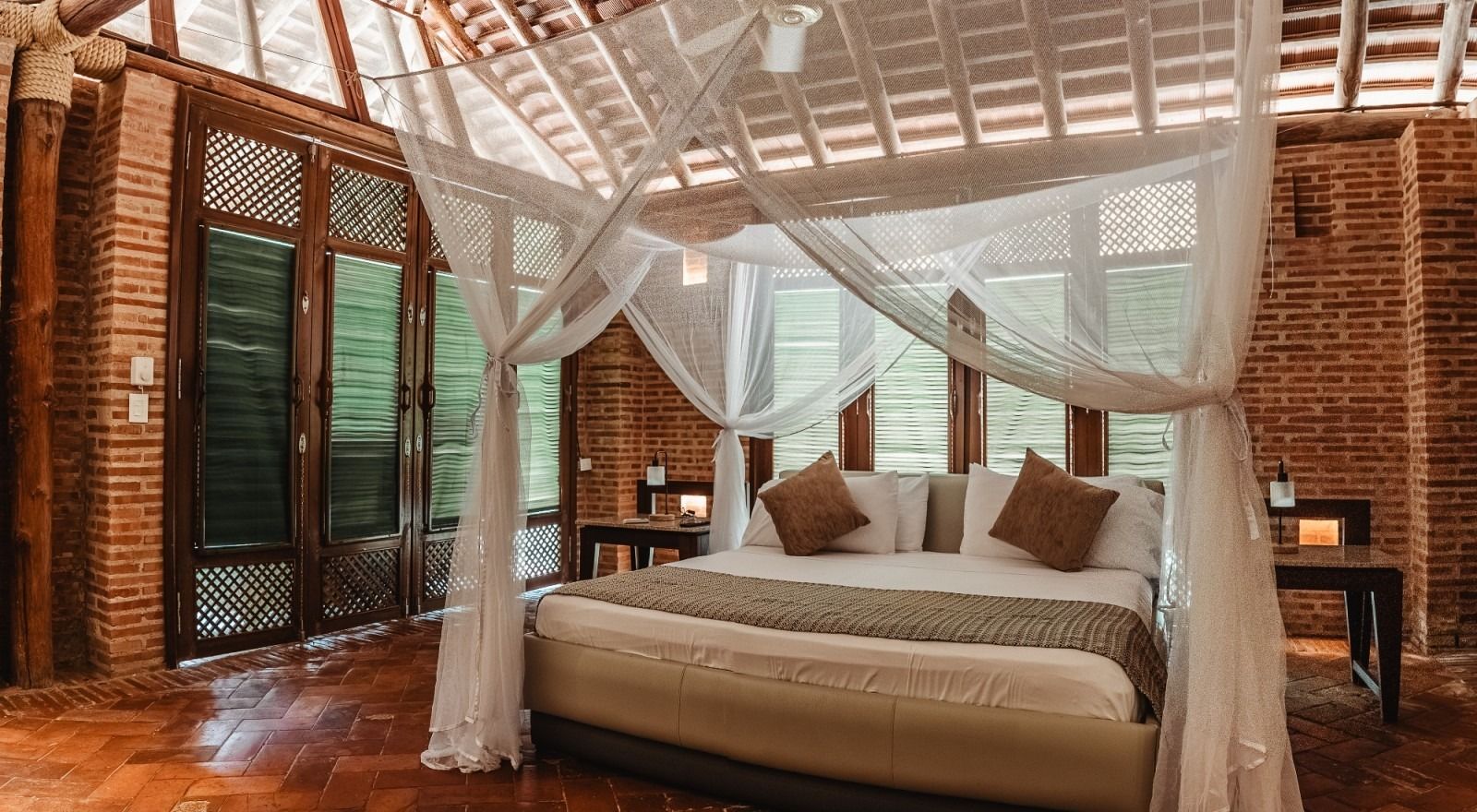 Bedroom with canopy bed, brick walls, wooden floor, and large windows.