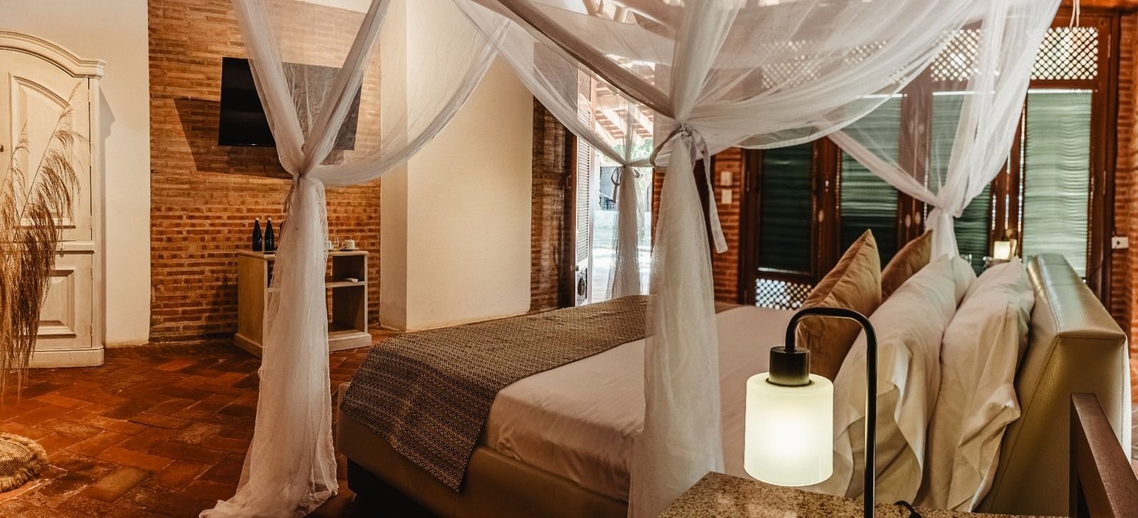 Bedroom with canopy bed, brick walls, hardwood floor, and a lamp.