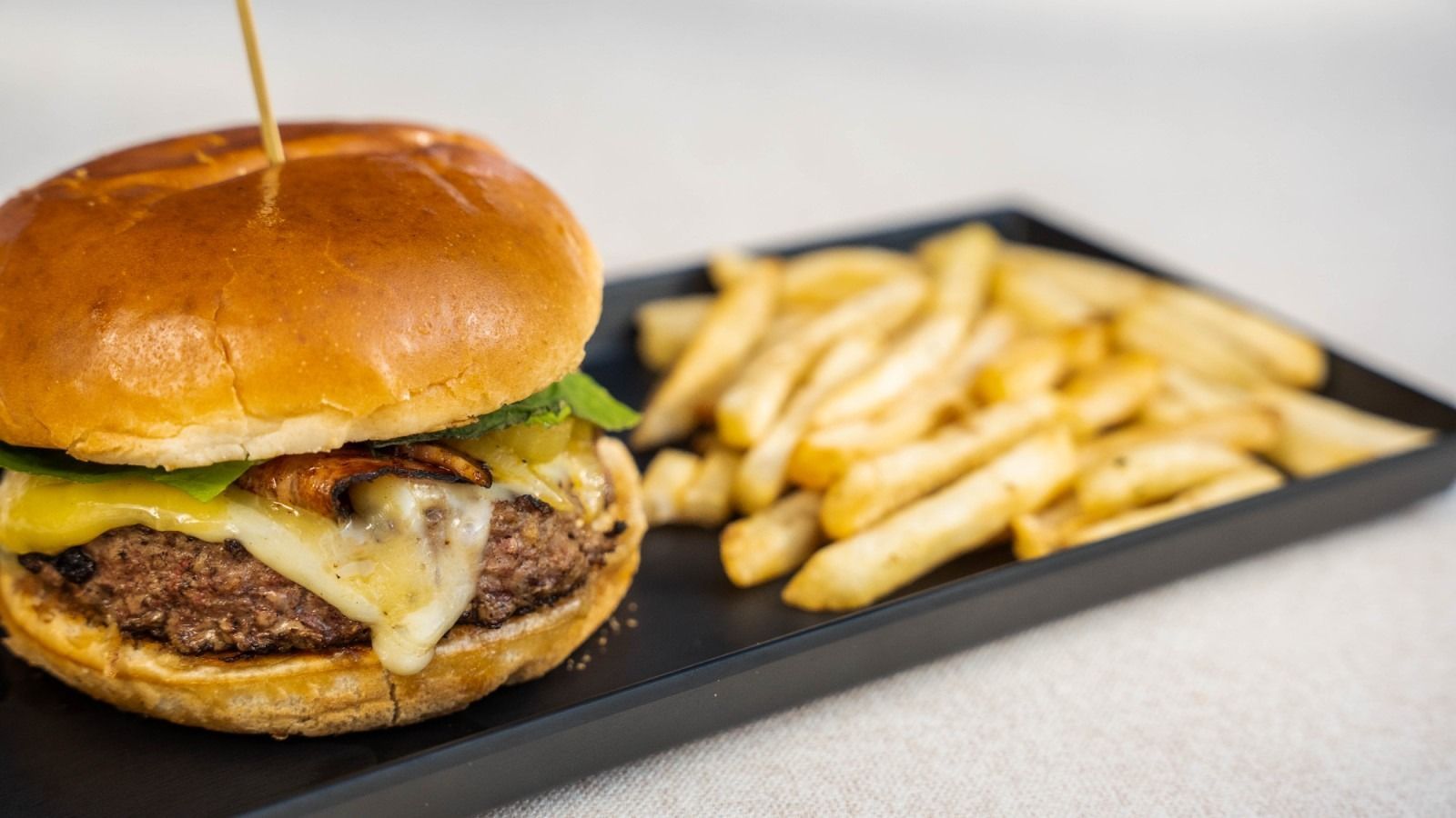 Burger with melted cheese, arugula, and fries on a black plate, held together with a toothpick.