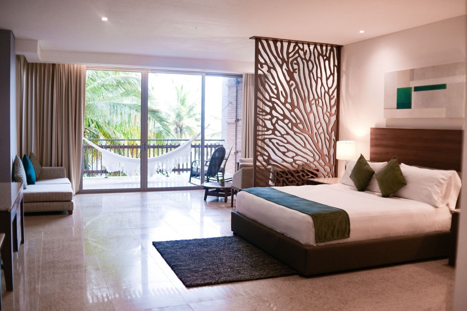 Spacious hotel room with king-size bed, balcony with hammock and ocean view, neutral tones.