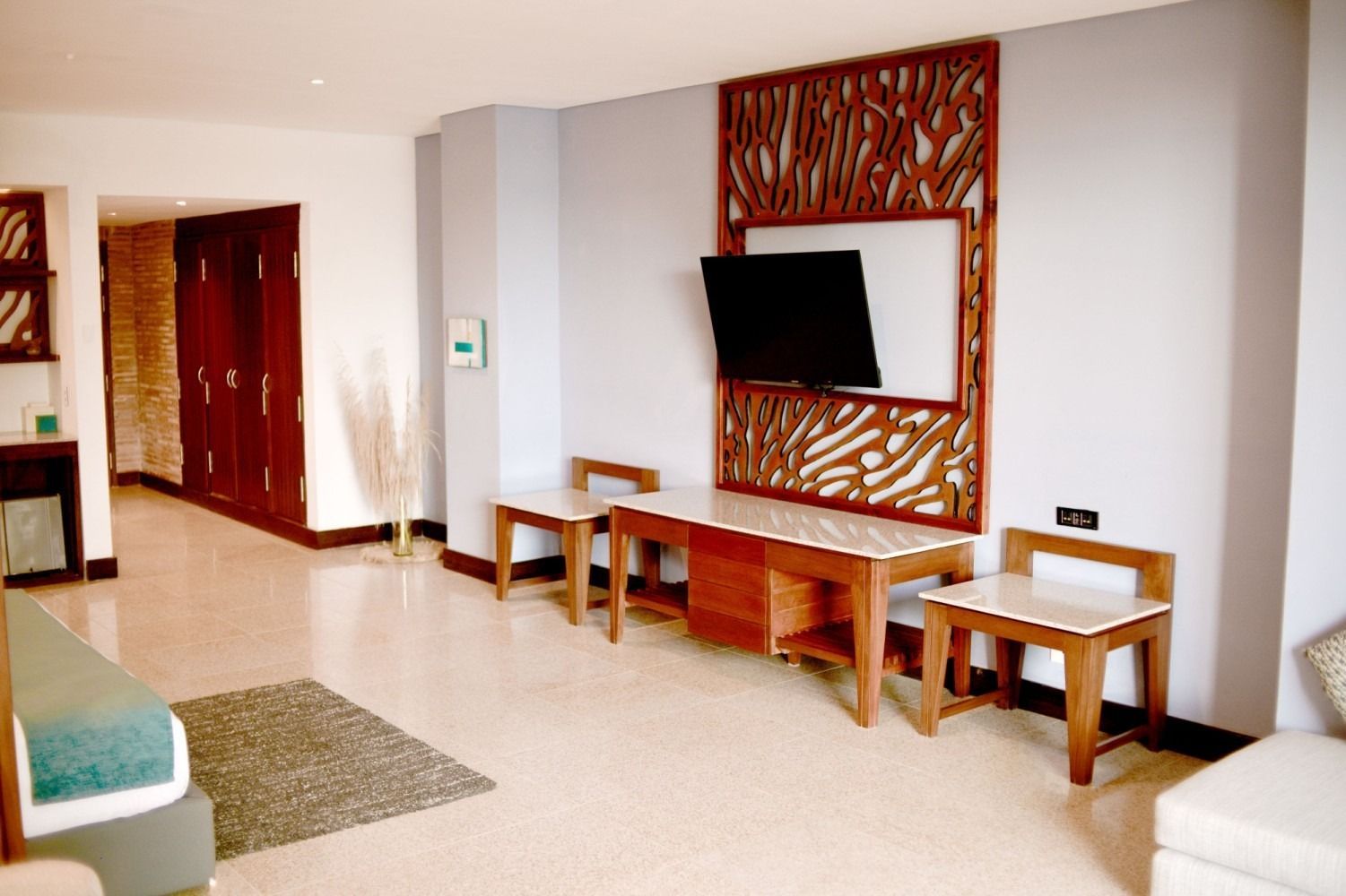 Spacious hotel room with TV, wood paneling, desk, chairs, and large closet. Pale walls and floor.