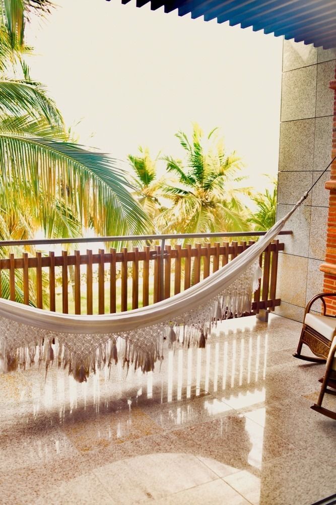 Hammock on a sunny balcony overlooking palm trees.