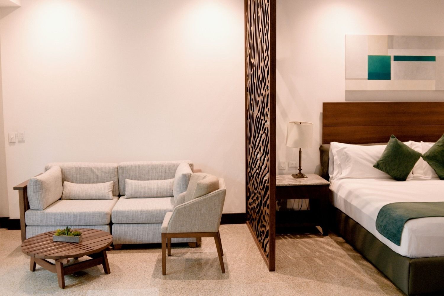 Hotel room with a bed, couch, chair, coffee table, and decorative wooden screen.