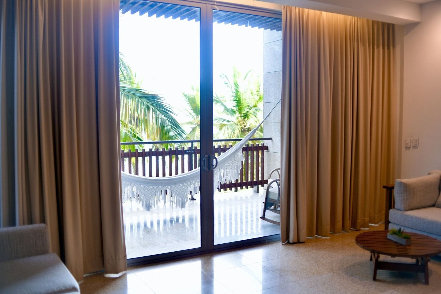 Interior view of a room with open sliding glass doors leading to a balcony with a hammock; beige curtains.