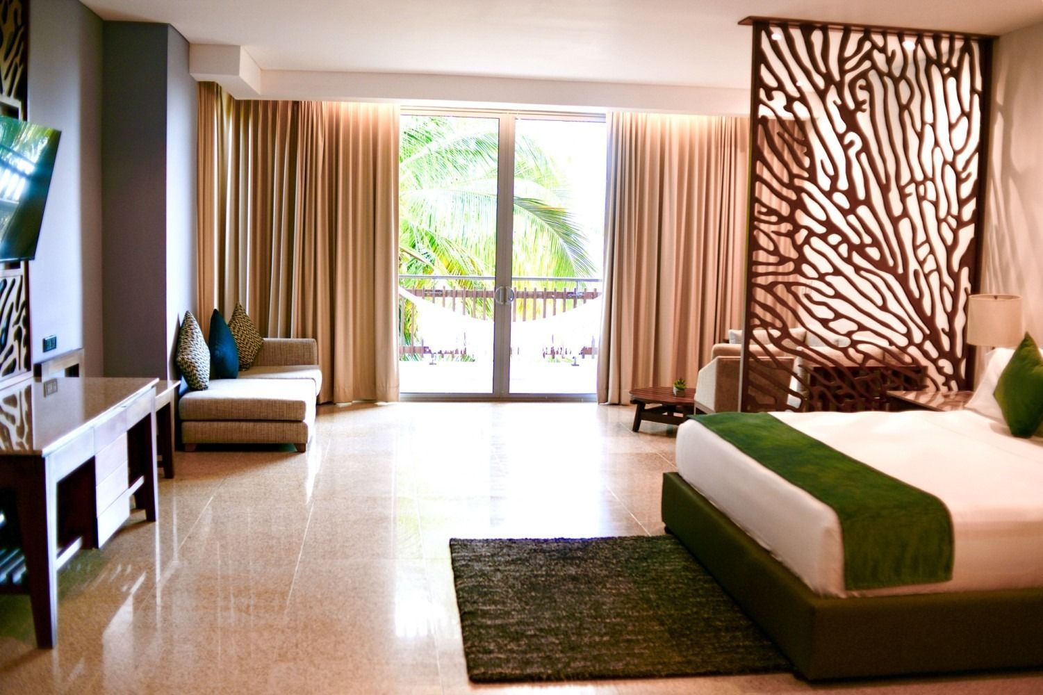 Spacious hotel room with king bed, balcony view, and decorative wood screen. Beige and green color scheme.