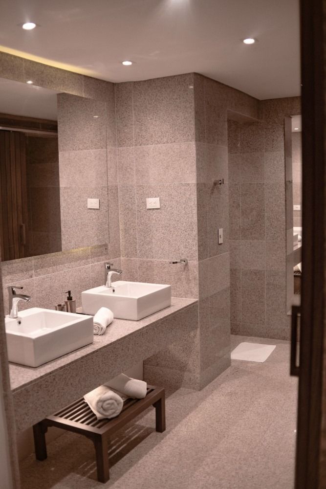 Bathroom with two white sinks, stone walls, towels, and a shower area.