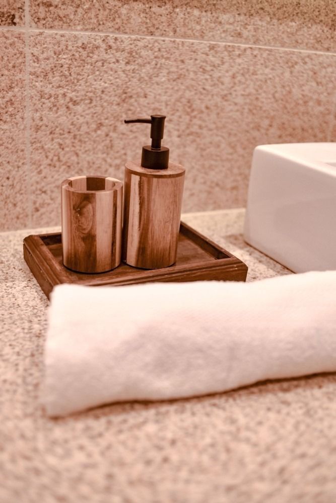 Wooden soap dispenser, cup, and tray on a speckled countertop with a white towel.