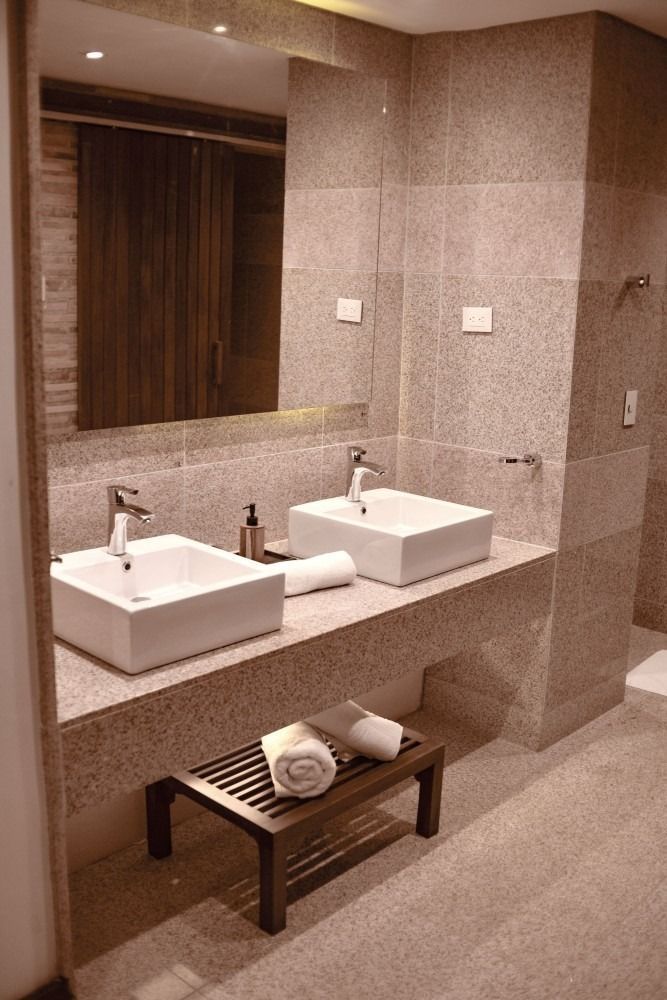 Bathroom with two white sinks, light gray walls, dark wood bench with towels.