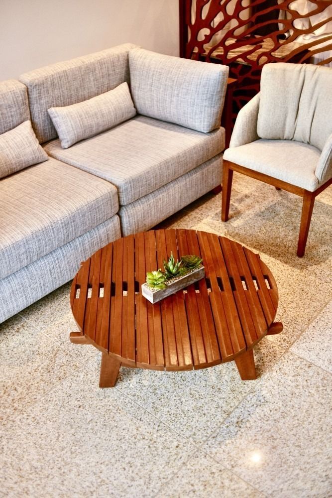 A modern living room with a light gray sectional, wooden chair, and round wooden coffee table.