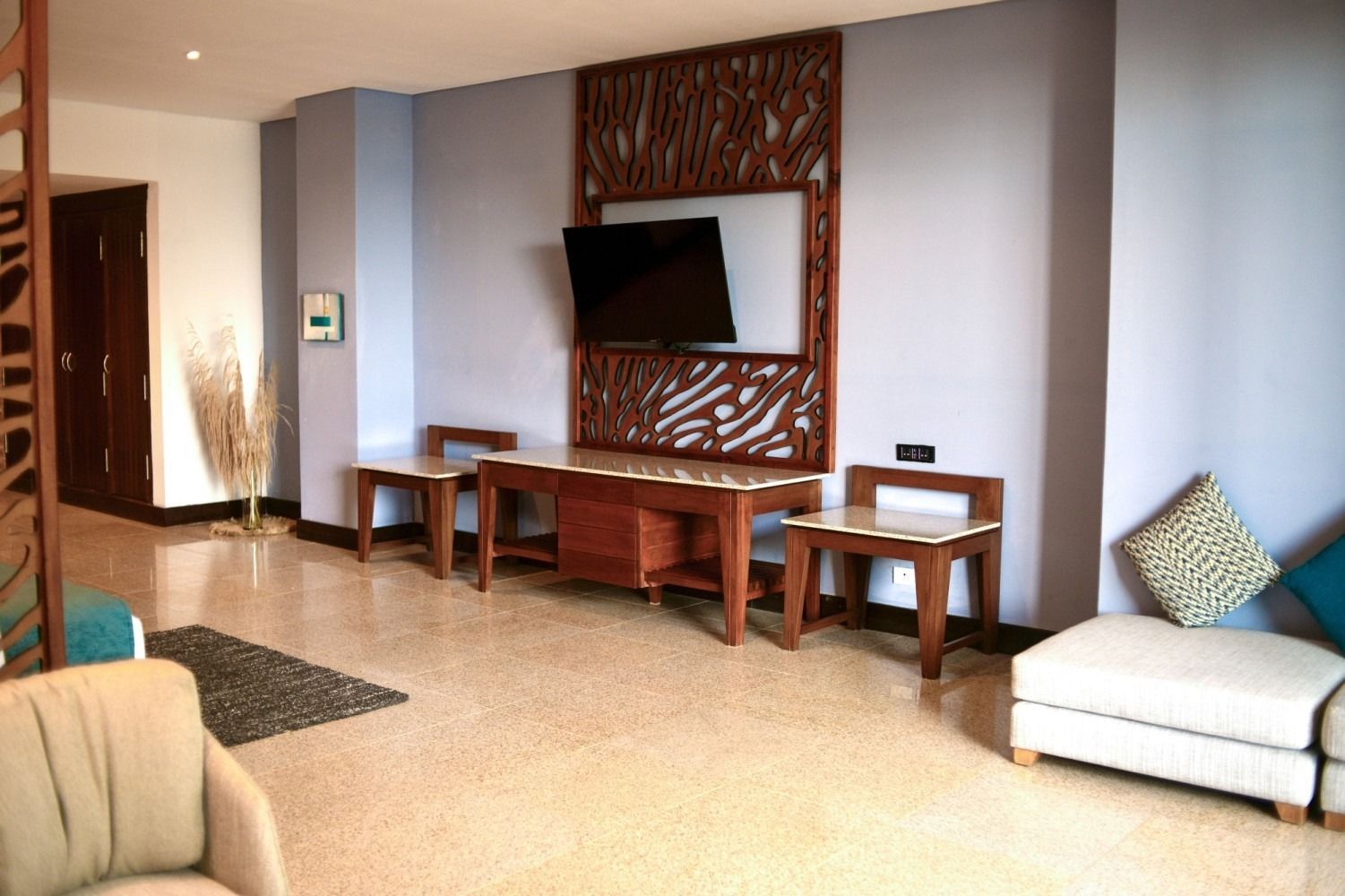 Living room with TV mounted on a decorative wall panel, two small benches, and a cream-colored sofa.