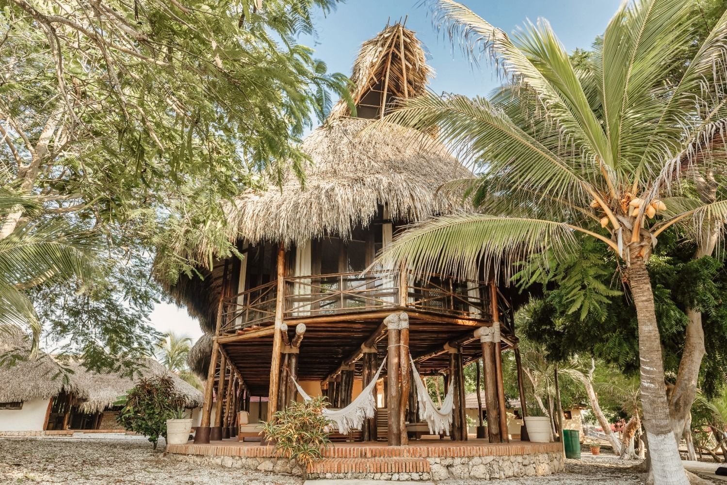 Tropical, two-story wooden structure with thatched roof, palm trees, and hammocks.