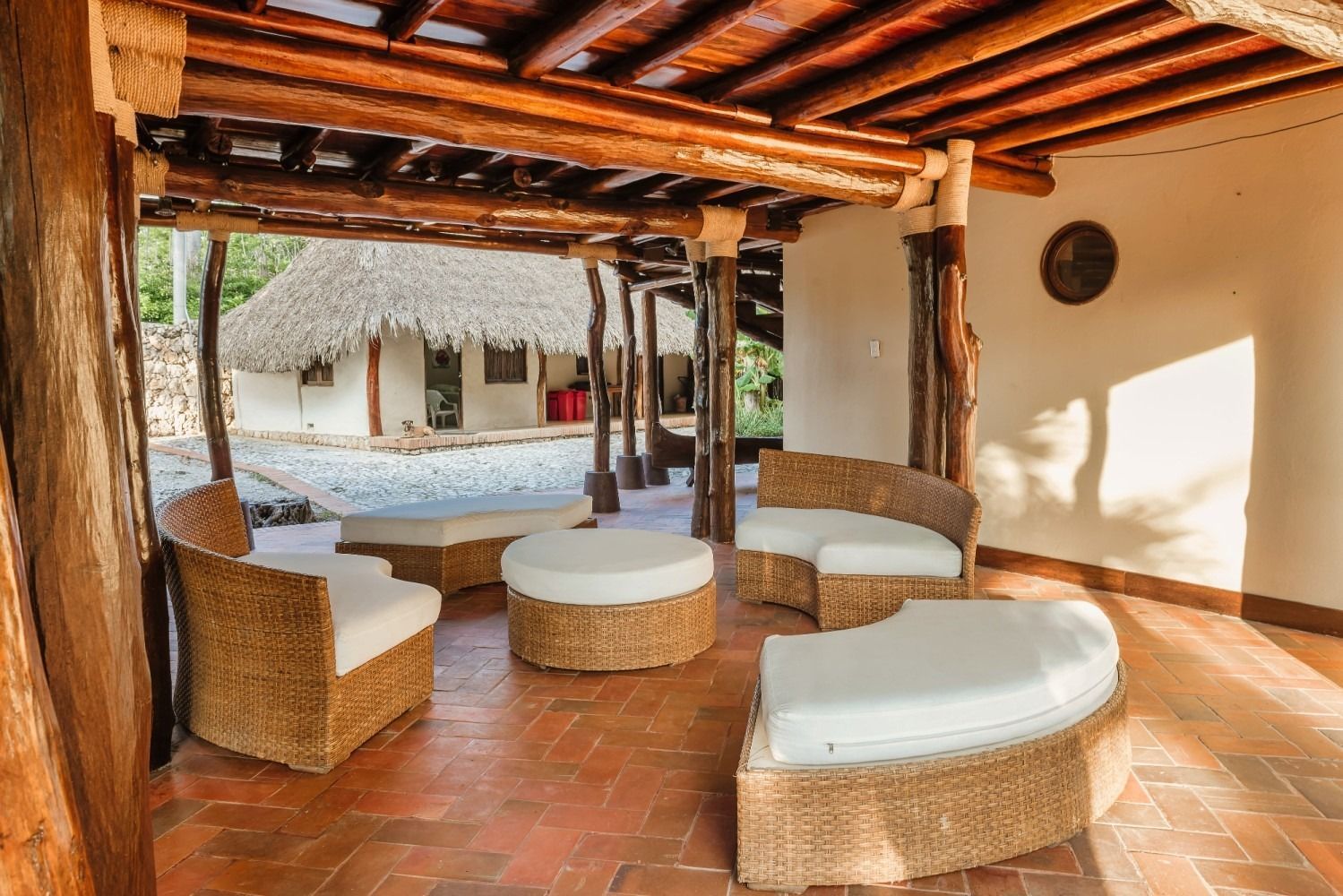 Covered outdoor seating area with wicker furniture and thatched roof in a tropical setting.