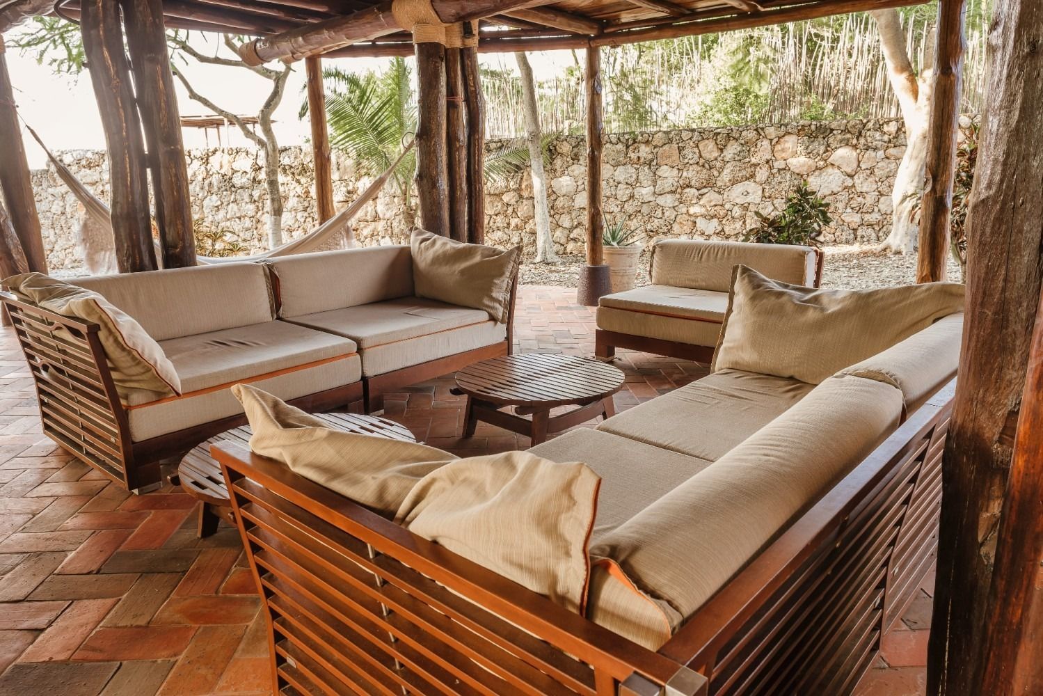 Outdoor seating area with wood sofas, coffee table, and stone wall backdrop.