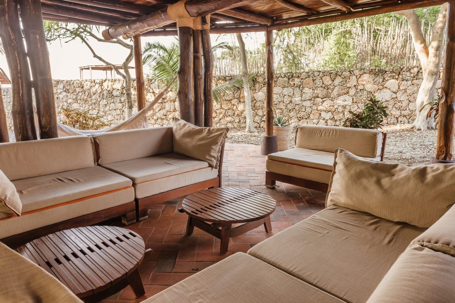 Outdoor seating area with beige cushions, wooden furniture, and a stone wall.