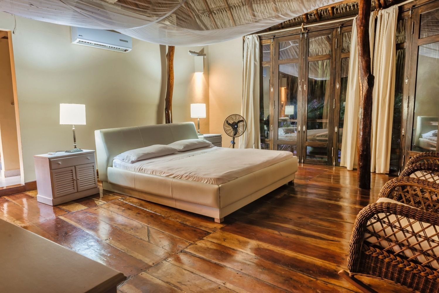 Bedroom with a low white bed, bedside lamps, wooden floors, and woven furniture.