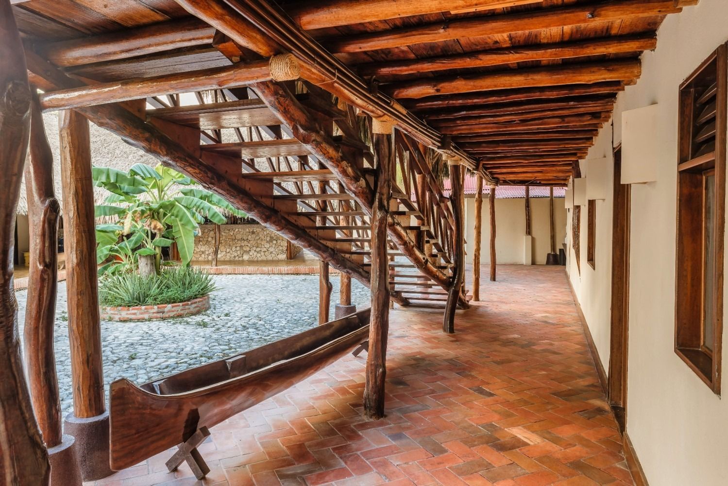 Wooden staircase and walkway with a tiled floor, overlooking a courtyard with plants.