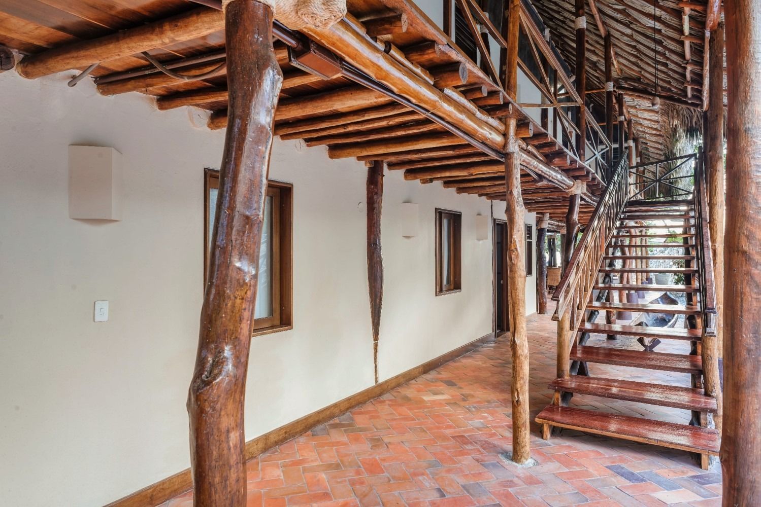 Covered walkway with wooden beams, red brick floor, and staircase leading up.