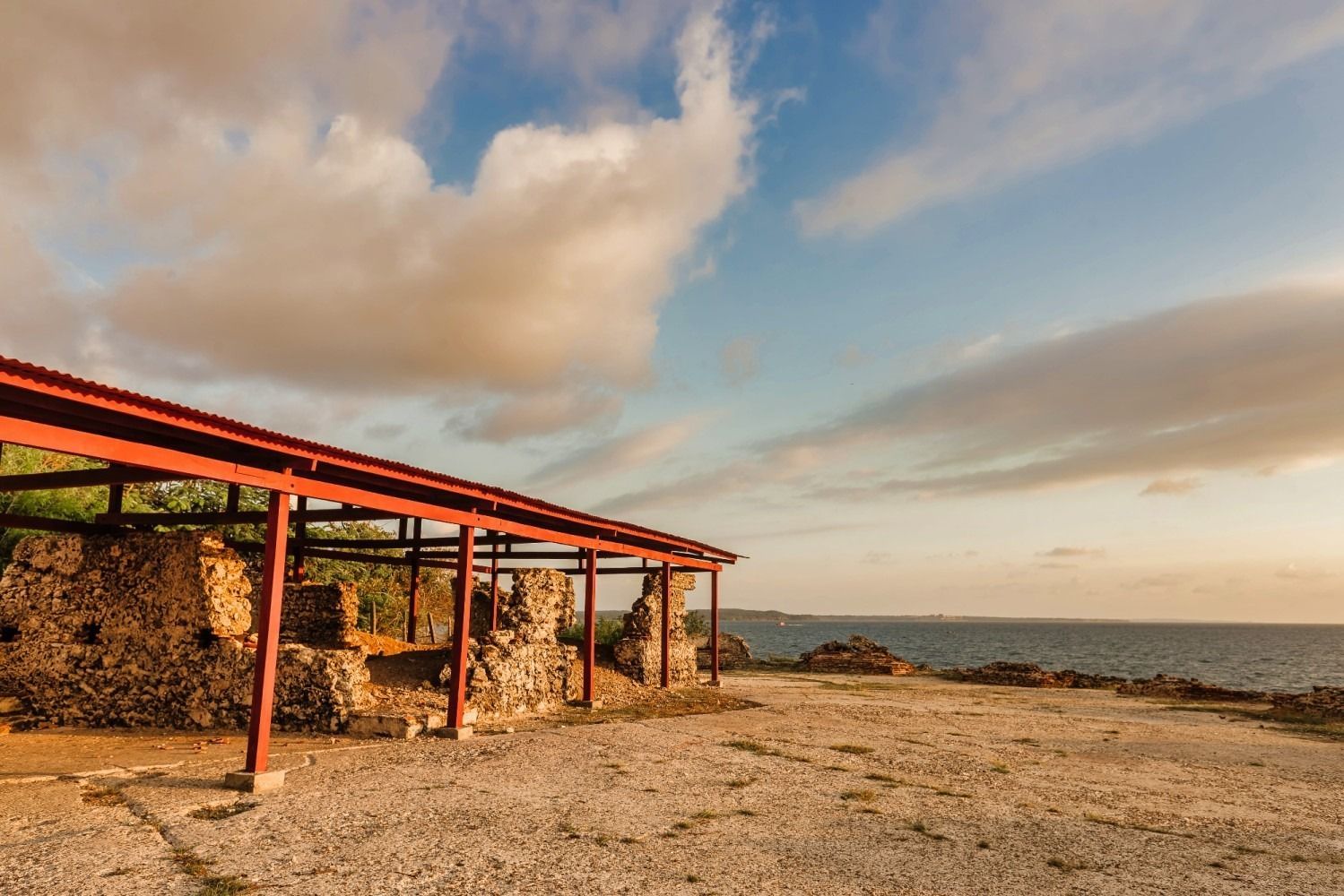 Ruined stone structure with red roof overlooking the ocean, under a cloudy sky.