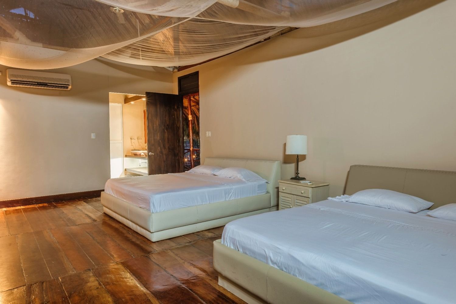 Bedroom with two beds, wooden floor, cream walls, and draped ceiling fabric.