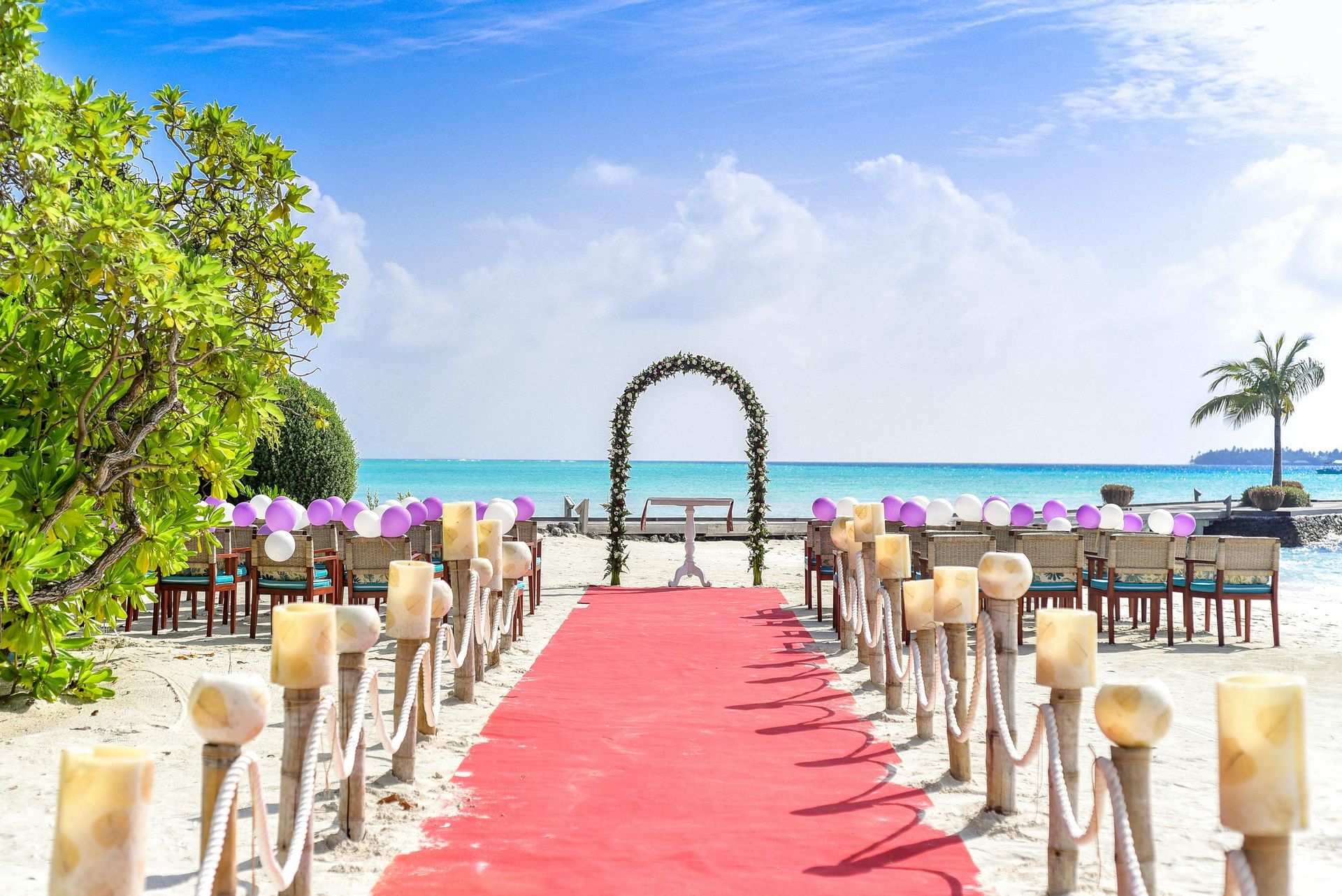 Wedding ceremony on a beach with red carpet, chairs, arch, and ocean view.