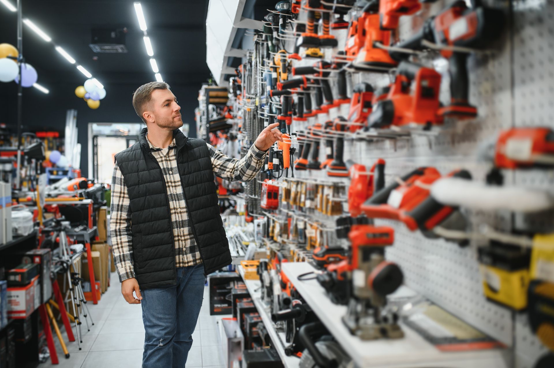 Man shopping for tools in a hardware store; browsing a wall display of tools. Man shopping for tools in a hardware store; browsing a wall display of tools.