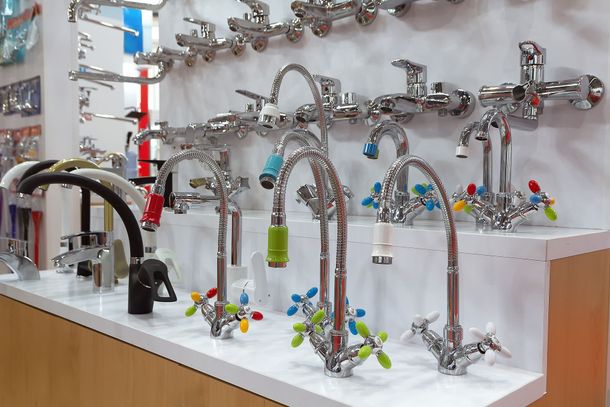 Display of various chrome faucets in a store setting, featuring several designs with colorful handles. Display of various chrome faucets in a store setting, featuring several designs with colorful handles.