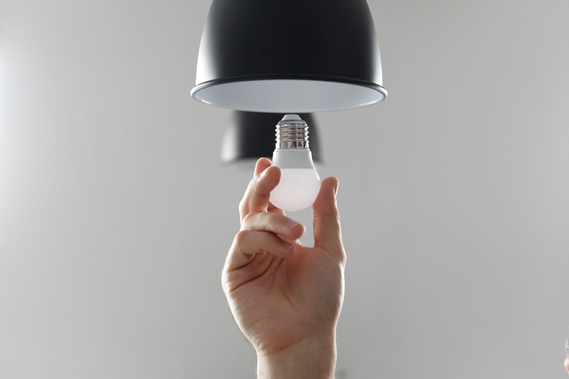 Hand holding a lightbulb under a black lampshade.