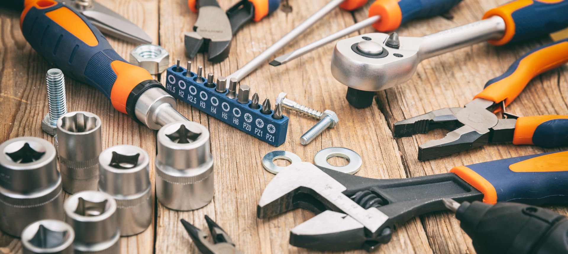 Assortment of tools, including wrenches, pliers, and sockets, on a wooden surface.